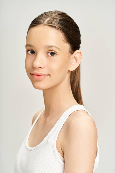 Een jong tienermeisje met een stijlvolle uitstraling poseert vol vertrouwen in een wit topje, straalt gratie en charisma uit. - Foto, afbeelding