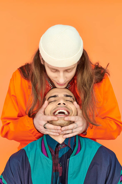 Jongeman knuffelen zijn vriendjes hoofd op oranje achtergrond. - Foto, afbeelding