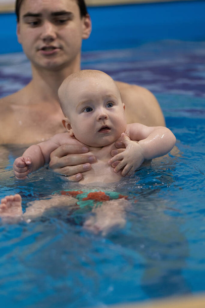 Portrait of the curious baby with a swim coach in a swimming pool. Swimming lessons for newborns - Photo, Image