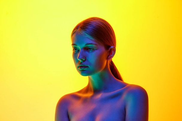 Giovane donna attraente posa con spalla nuda posa guardando lontano in luce al neon contro sfondo studio gradiente. Concetto di bellezza naturale, cosmetici biologici, procedure termali, cura del viso. - Foto, immagini