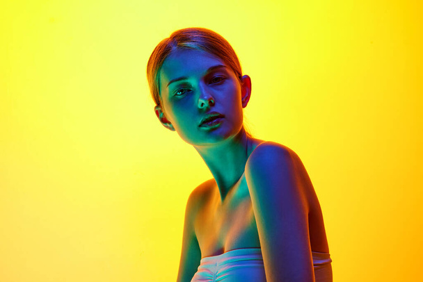 Atraktivní mladá žena na vrcholu vypadá sebevědomě na kameru ve smíšeném neonovém světle na pozadí gradientu studia. Pojem přírodní krásy, organická kosmetika, lázeňské procedury, péče o obličej. - Fotografie, Obrázek