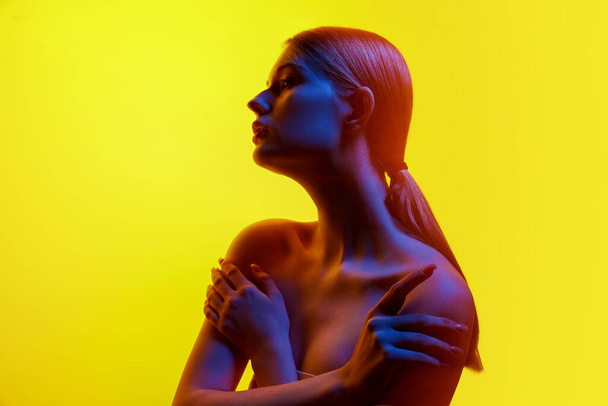 Portrét mladé ženy, která ukazuje svou něhu, dívá se stranou a položí ruce na ramena v neonovém světle na pozadí svahu. Pojem přírodní krásy, organická kosmetika, lázeňské procedury. - Fotografie, Obrázek