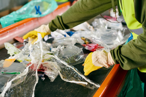 A young volunteer in a green shirt cleans a table, part of a group sorting trash in safety vests, promoting sustainability. - Foto, afbeelding