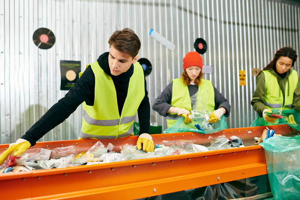 Young volunteers in gloves and safety vests sort trash on a conveyor belt, promoting eco-consciousness. - Fotoğraf, Görsel