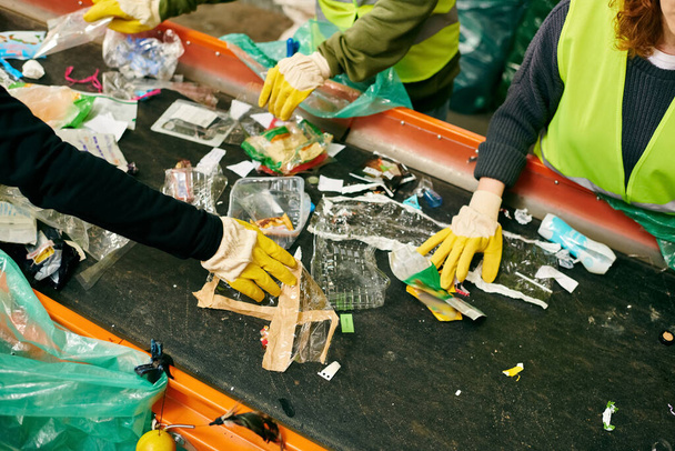 Young volunteers in safety vests sort through heaps of garbage on a table, united by a mission to clean up the environment. - Фото, изображение