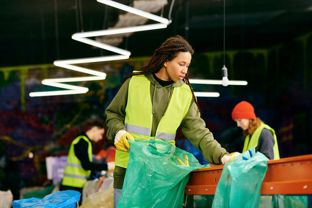 A young volunteer in a green vest is holding a bag while sorting trash with other eco-conscious people. - Photo, image