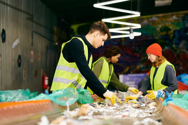 Young volunteers in gloves and safety vests sort trash in a room, demonstrating their eco-conscious behavior. - Zdjęcie, obraz