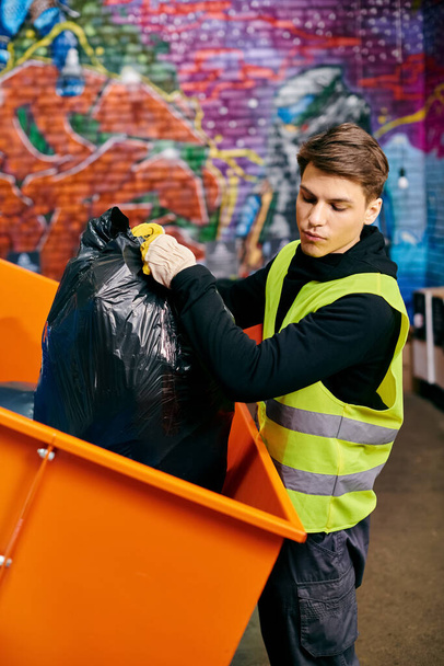 A young volunteer in a yellow vest carefully holds a trash can while sorting waste - Zdjęcie, obraz
