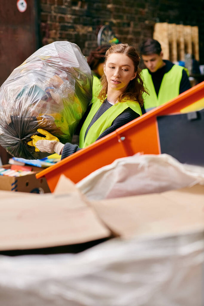 Young eco-conscious volunteers in gloves and safety vests sorting trash together around a pile of boxes. - Fotó, kép