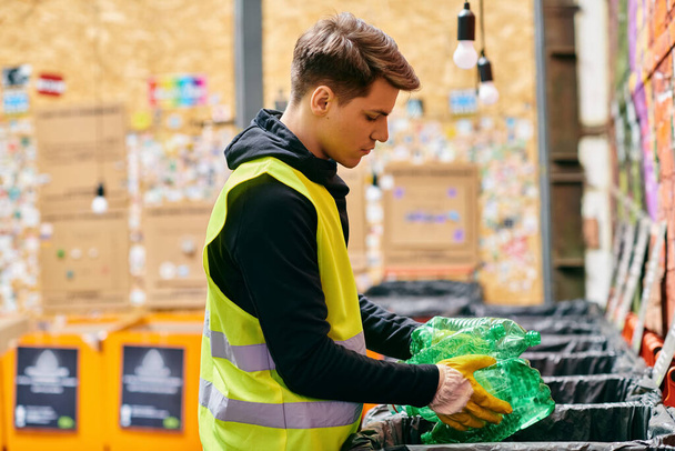 A young eco-conscious man in a yellow vest sorting garbage while volunteering with others in gloves in an outdoor park. - Фото, изображение