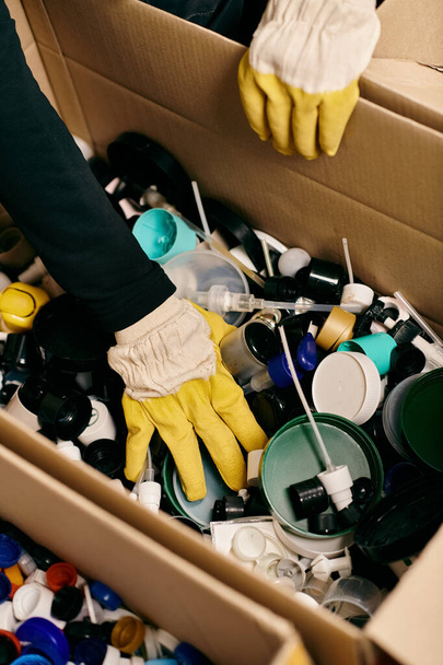 A young volunteer in gloves and a safety vest, sorting through a box filled with a wide variety of items. - Foto, Imagem