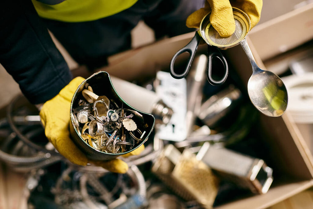 A passionate young volunteer, dressed in yellow gloves, holds a pair of scissors while sorting waste as part of an eco-conscious initiative. - Foto, Imagen