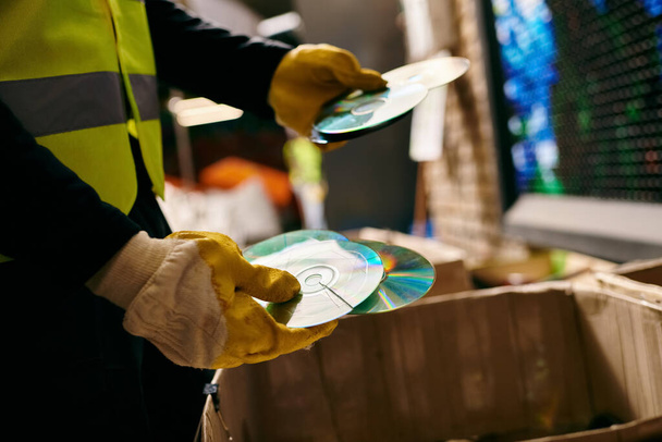 A young volunteer in a yellow safety vest sorts waste, holding cd with eco-conscious intentions. - 写真・画像