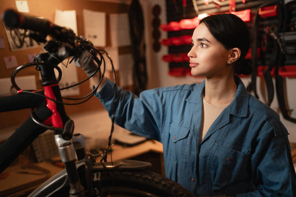 Велосипед механічної перевірки велосипеда в майстерні або гаражі. Молода зосереджена біла жінка. Велосервіс, ремонт та оновлення концепції. Інтер'єр гаража. Копіювати простір - Фото, зображення