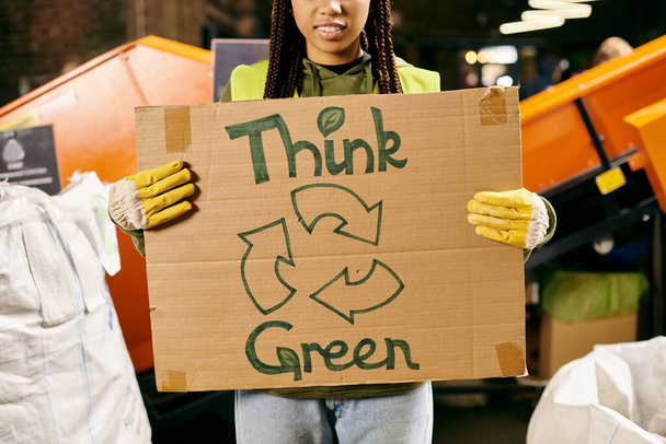 A young volunteer in gloves and safety vest holds a sign saying think green, promoting environmental awareness through action. - 写真・画像