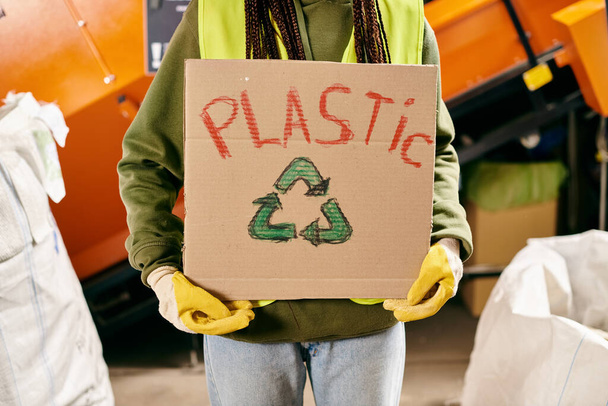A young volunteer in gloves and safety vest holding a cardboard sign that says plastic. - Photo, image