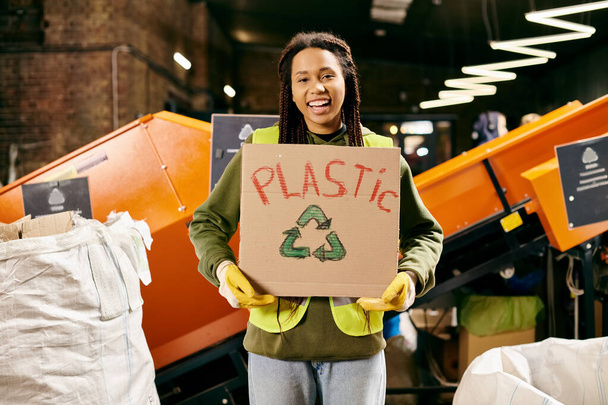 Young volunteer in safety gear sorting waste, holding a sign that says plastic. - Φωτογραφία, εικόνα