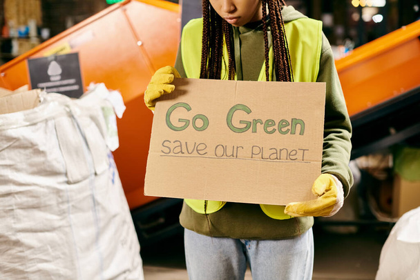 A young volunteer in gloves and a safety vest holds a sign urging to go green and save our planet. - Valokuva, kuva