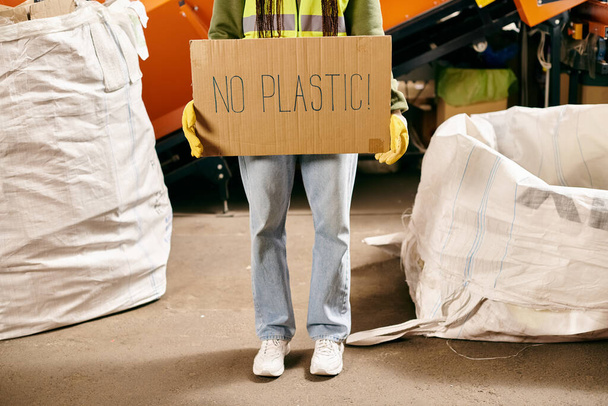 Young volunteer in gloves and safety vest holds sign that says no plastic while sorting waste. - Fotoğraf, Görsel