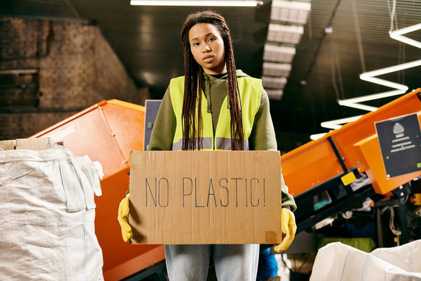 Young volunteer in gloves and safety vest holding a sign that says no plastic while sorting waste. - Fotoğraf, Görsel