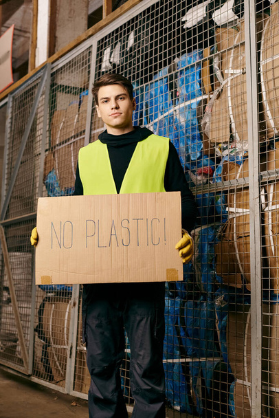 A young volunteer in gloves and safety vest sorts waste, passionately displaying a no plastic sign. - Valokuva, kuva