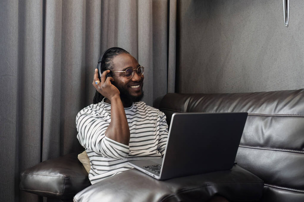 Afroamerykanin relaksujący się na kanapie i słuchający muzyki w domu. - Zdjęcie, obraz