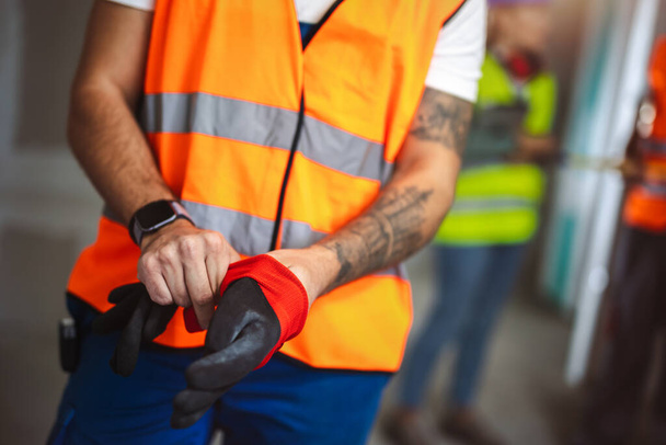 Trabajador de la construcción se pone guantes en un sitio de construcción. - Foto, imagen