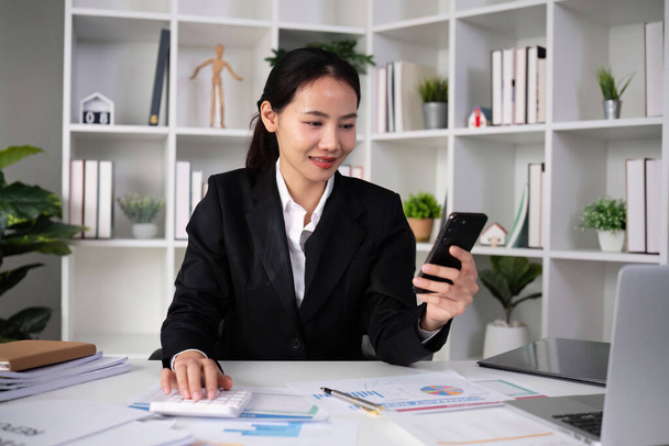 Ázsiai női könyvelő Használjon számológépet, hogy kiszámítsa az üzleti számokat egy fehér fa asztal az irodában.. - Fotó, kép