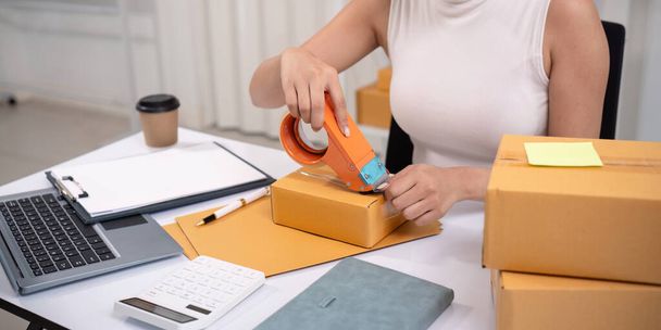 Woman asian use scotch tape to attach parcel boxes to prepare goods for the process of packaging, shipping, online sale internet marketing ecommerce concept startup business idea. - Photo, Image