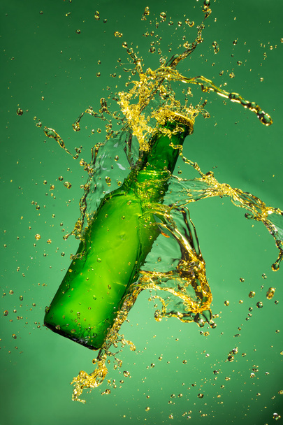 Green beer bottle with splashing liquid - Foto, afbeelding