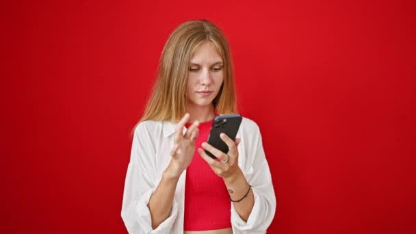 Heyecanlı, sarı saçlı genç bir kadın canlı kırmızı bir arka plana karşı akıllı telefon içeriğine tepki veriyor.. - Video, Çekim