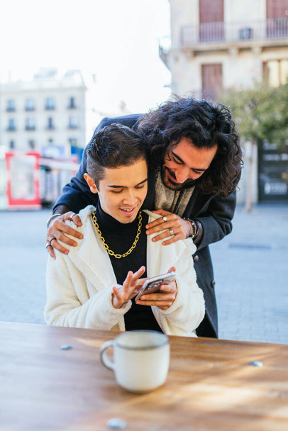カフェでスマートフォンでコンテンツを共有するゲイカップルの間の愛情の瞬間 - 写真・画像