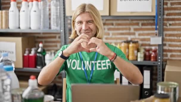 Mosolygós férfi önkéntes pólóban, aki laptopon dolgozik egy raktárban.. - Felvétel, videó