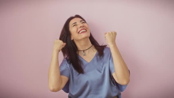 Femme hispanique d'âge moyen exorbitante acclamant dans la victoire, levant fièrement les bras, debout sur fond rose isolé, rayonnant de joie avec des cris de succès excités. - Séquence, vidéo