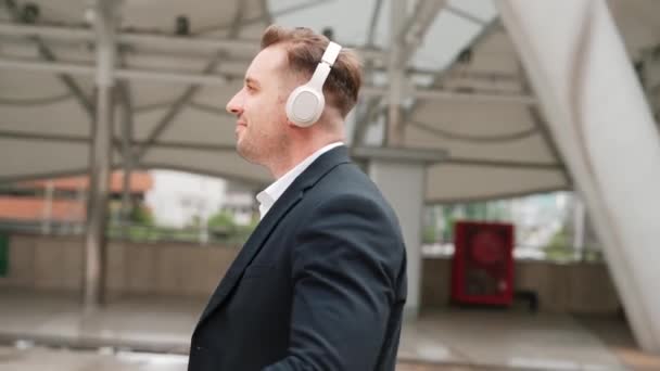 Happy business man using headphone listening relax music and move along music while walking at street in urban city with lively mood. Manager wear headset and enjoying listen relaxing rhyme. Urbane. - Footage, Video