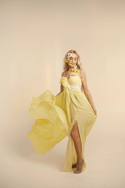 Beautiful woman in yellow flying dress with chrysanthemums - Photo, Image