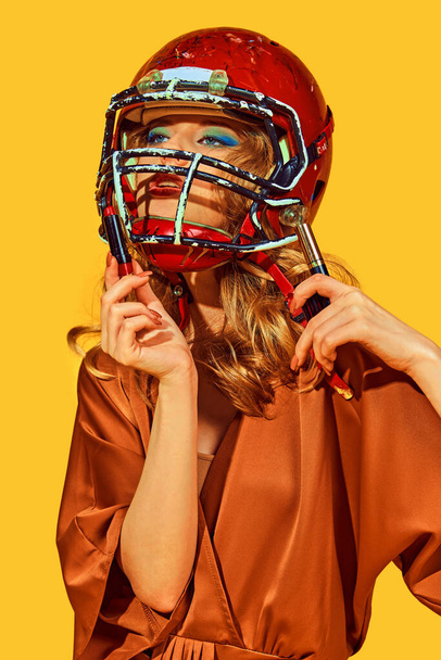 Retrato de mujer en traje elegante con casco de fútbol hace maquillaje contra fondo de estudio amarillo. Concepto de mujer en fútbol, deporte y moda, estilo y belleza. Anuncio - Foto, imagen