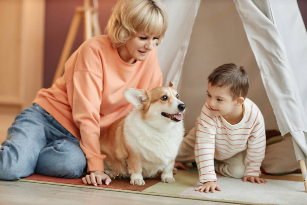 Down sendromlu küçük çocuk evde anne ve köpekle oyun oynuyor. - Fotoğraf, Görsel