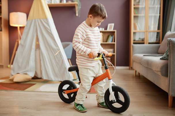 Portrait of little boy with down syndrome learning to use runbike indoors - Photo, Image