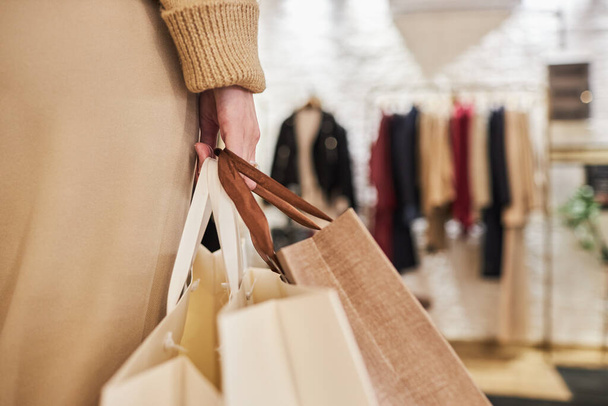 Nahaufnahme einer nicht wiederzuerkennenden jungen Frau, die beim Einkaufen im Bekleidungsgeschäft Taschen mit Einkäufen in der Hand trägt, Kopierraum - Foto, Bild