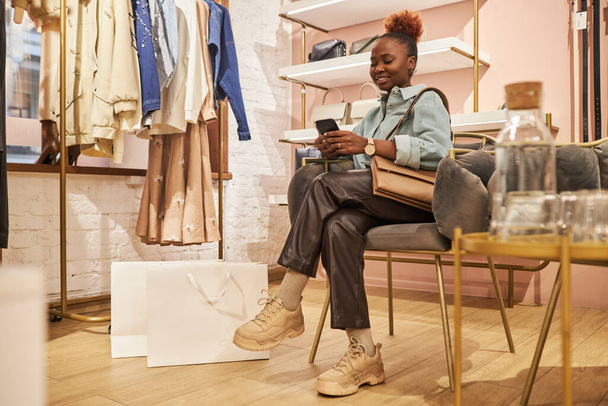 Full length portrait of black young woman using smartphone in clothing boutique and using mobile app, copy space - Photo, Image