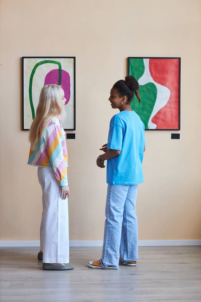 Вертикальный портрет двух девушек-подростков, обсуждающих картины в галерее современного искусства - Фото, изображение