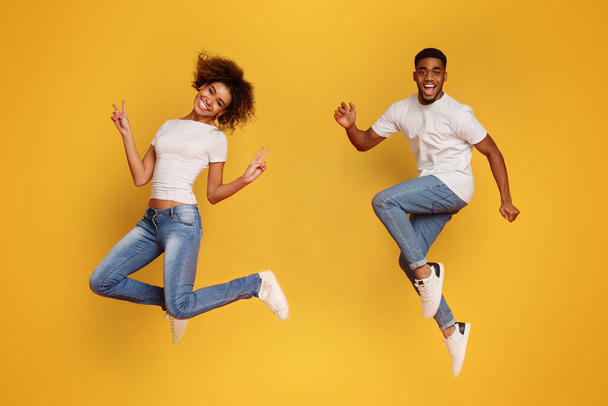 Alegre pareja afroamericana corriendo en el aire, saltando sobre fondo de estudio naranja
 - Foto, imagen