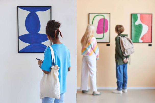 Back view at diverse group of teenagers looking at abstract art in modern art gallery or museum, copy space - Photo, Image