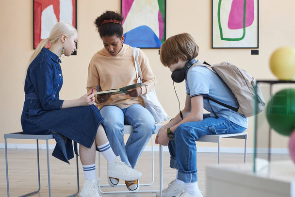 現代美術館や博物館で学校のプロジェクトをしているサークルに座っている3人のティーンエイジャーのグループ - 写真・画像
