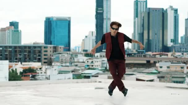 Танцевальное выступление B-boy от профессиональной уличной танцовщицы на крыше с небоскрёбом, вид на город. Привлекательный азиатский хипстер показывает энергичный шаг. Активный танец. Открытый спорт 2024. Хипоп. - Кадры, видео