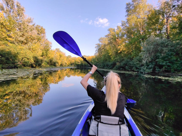 A young blonde woman is paddling in a kayak. Rear view. Tourism, sports and outdoor recreation - Photo, Image