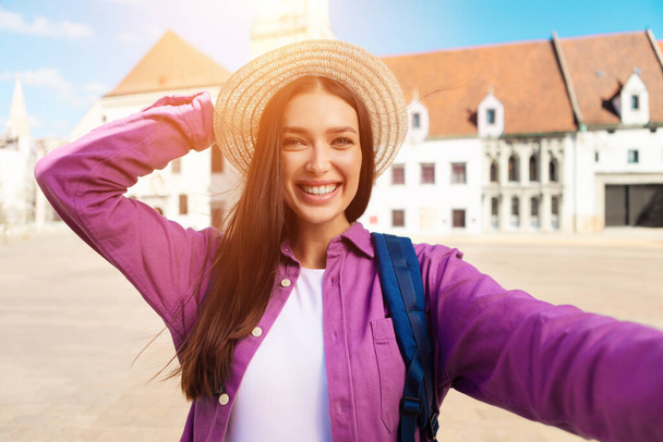 Una giovane studentessa scatta un selfie giocoso all'aperto, mettendo in mostra il suo stile di vita millenario contro l'architettura del patrimonio europeo - Foto, immagini