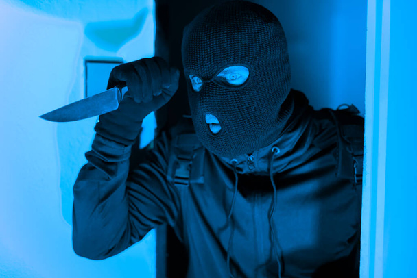Драматичне зображення, що показує маскований грабіжник, дивлячись навколо дверей, ножем в руці, що уособлює жах крадіжки злодія з квартири під прикриттям ночі - Фото, зображення