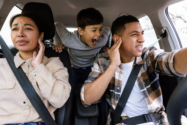 Jeune garçon criant, se sentant en colère, parents couvrant les oreilles tout en voyageant ensemble en voiture, ayant des conflits familiaux pendant le voyage en voiture - Photo, image
